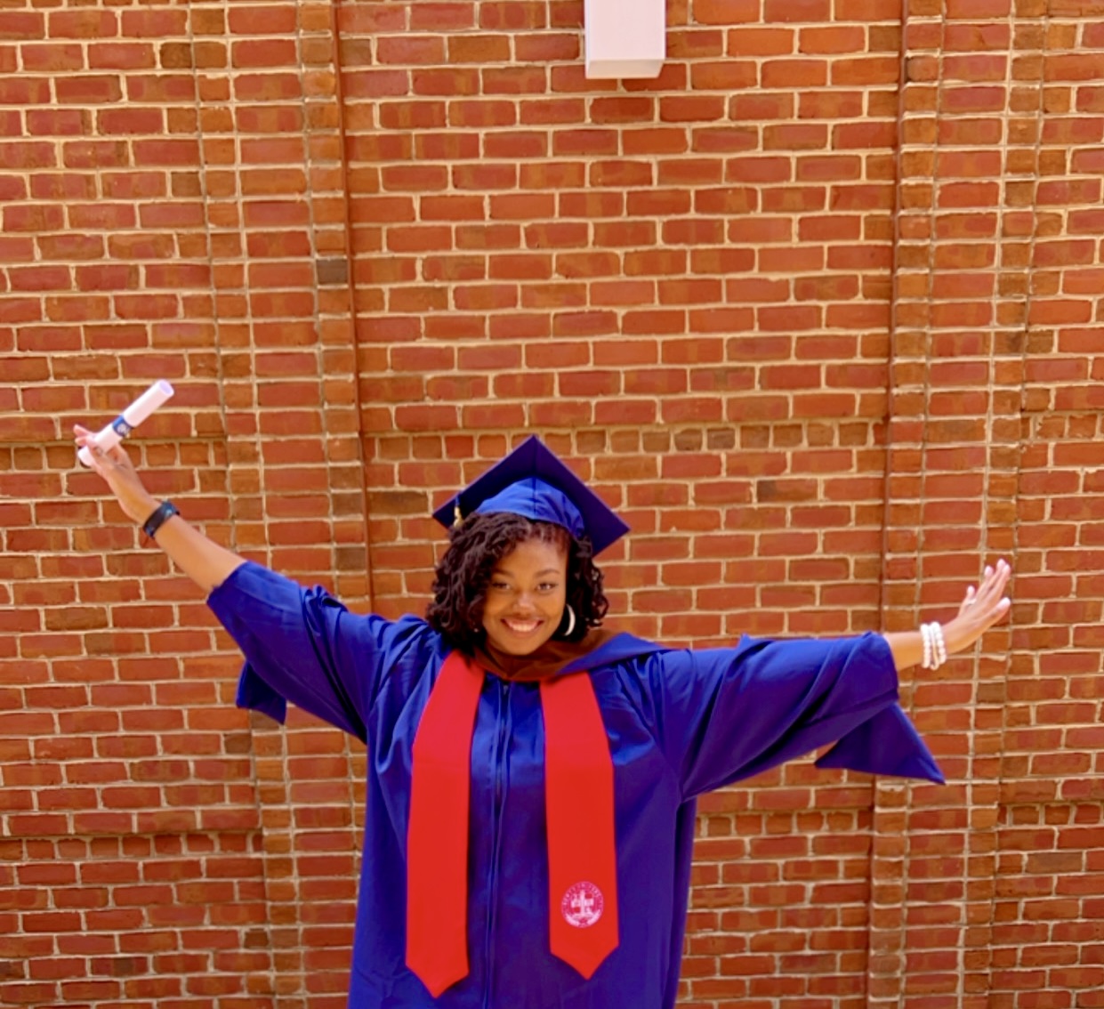 Brenisha celebrating her graduation with arms outstretched in joy, diploma in hand, showcasing her enthusiasm and accomplishment