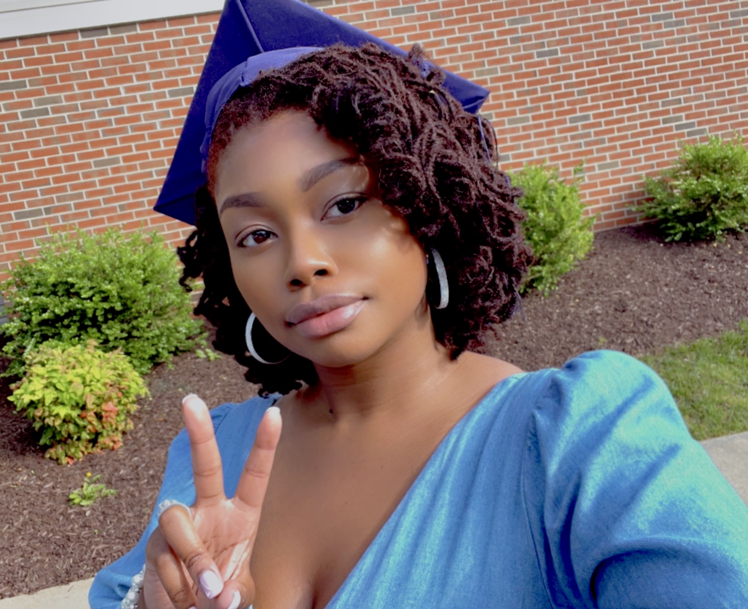 Close-up selfie of Brenisha in her graduation cap making a peace sign, capturing a moment of personal triumph and satisfaction